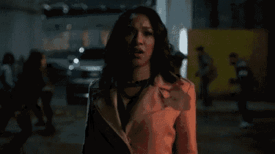 a woman in a white jacket is standing in a dark room with a car in the background .