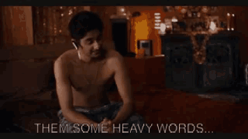 a shirtless man sits on a bed with the words " them some heavy words " above him