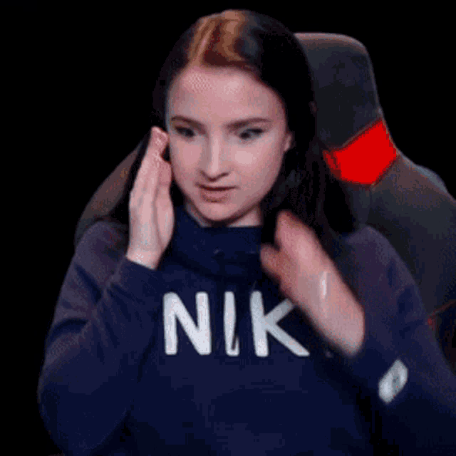 a woman wearing a blue nike sweatshirt is sitting in a chair covering her ears
