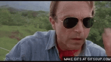 a man wearing sunglasses and a blue shirt is walking in a field .
