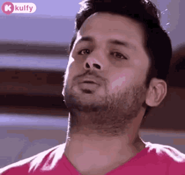 a man with a beard is wearing a pink shirt and looking at the camera .