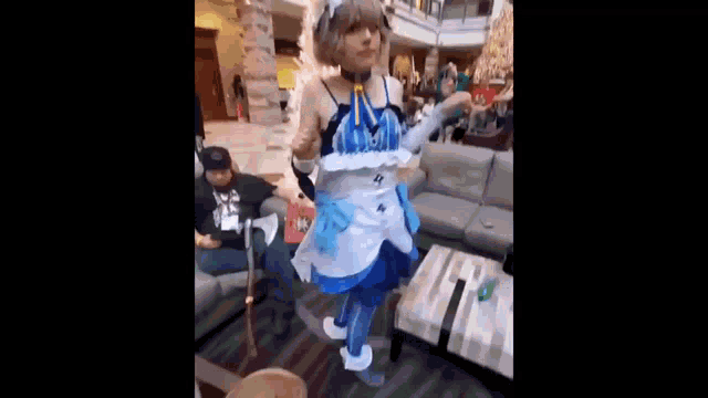 a person in a cosplay costume is dancing in a room with a man sitting on a couch .