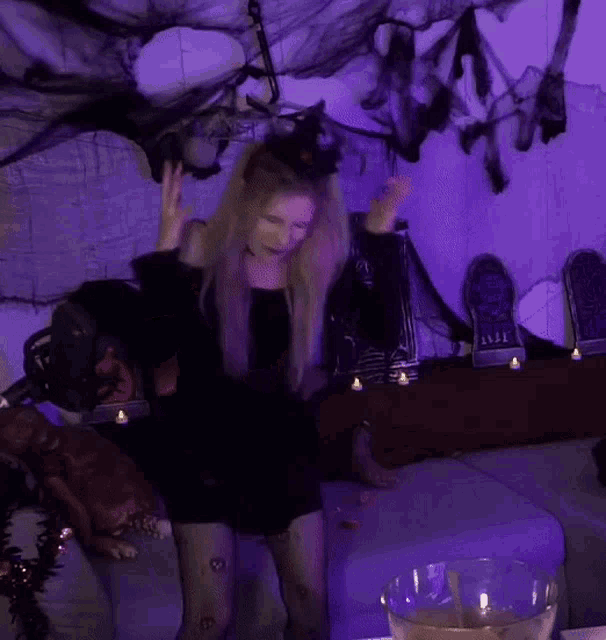 a woman in a black dress is dancing in front of a purple wall .