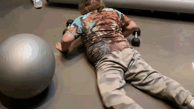a man is laying on the floor with a ball and dumbbells in the background