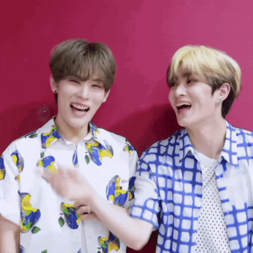 two young men are laughing together while wearing blue and white shirts against a red background .