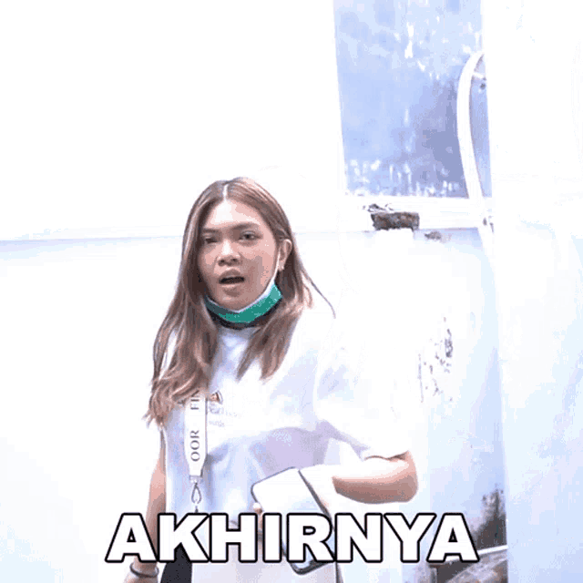 a woman wearing a mask is holding a cell phone and the word akhirnya is above her