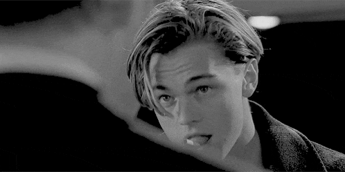 a black and white photo of a young man with long hair sticking his tongue out .