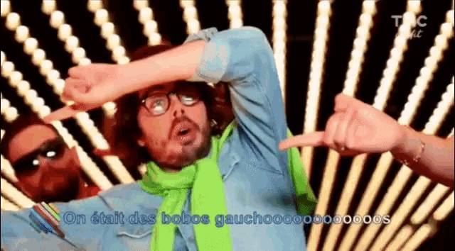 a man wearing glasses and a green scarf is dancing in front of a bunch of lights