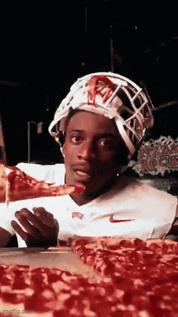 a man wearing a football helmet is eating a slice of pizza ..