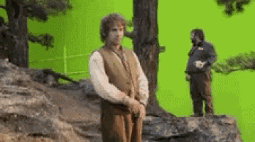 a man is standing on a rock in front of a green screen while another man stands behind him .
