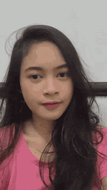 a woman with long black hair is wearing a pink t-shirt