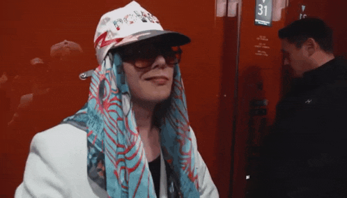 a woman wearing a hat and scarf stands in front of a red wall with a number 31 on it