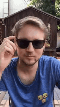 a man wearing sunglasses and a blue shirt with skulls on the pockets