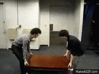 two men are lifting a wooden table in a room .