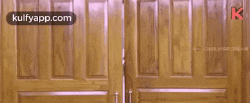 a man is peeking out of a wooden door with his hands outstretched .