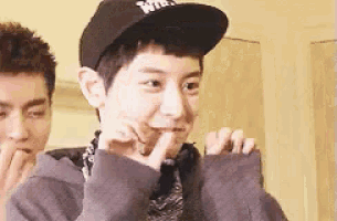 a young man wearing a black hat and a gray sweater is making a funny face .