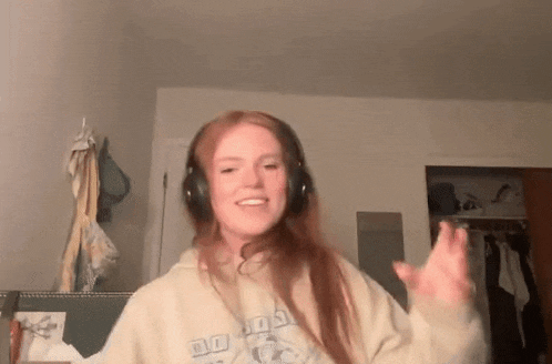 a woman wearing headphones and a hoodie is dancing in a bedroom .