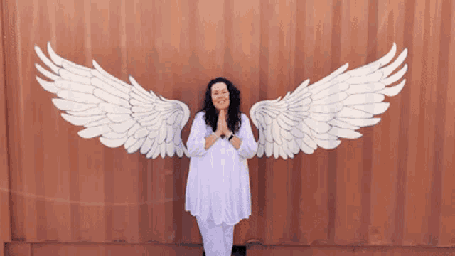 a woman in a white dress is standing in front of a wall with angel wings painted on it