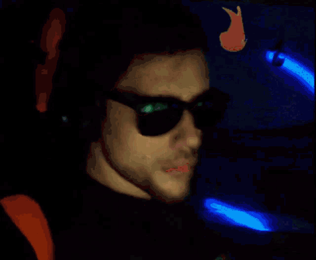a man wearing sunglasses and headphones is sitting in front of a neon sign that says " nenite "