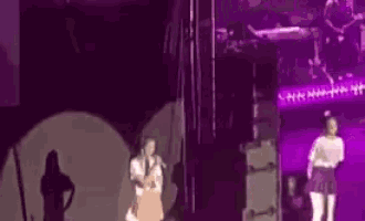 a couple of women are standing on a stage in front of a purple light .