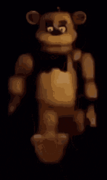 a brown teddy bear with a black bow tie is standing in the dark .