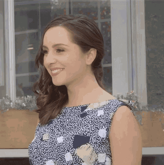 a woman in a blue and white polka dot dress smiles in front of a window