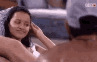 a man and a woman are sitting next to each other . the woman is touching the man 's hair .