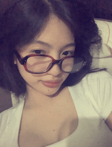 a woman wearing glasses and a white shirt is taking a selfie