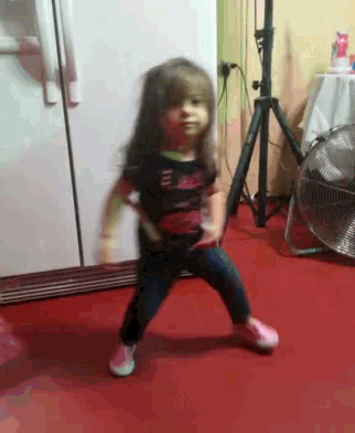 a little girl is dancing in front of a fan and a refrigerator