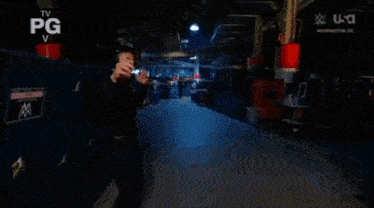 a man in a black tank top is standing in a dark room with a w logo on the screen .
