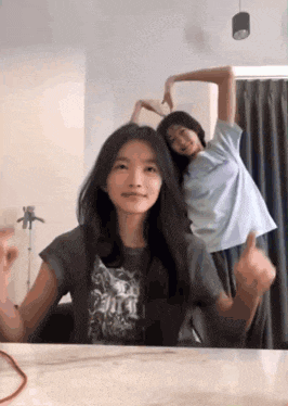 two girls are making a heart shape with their hands while standing next to each other .