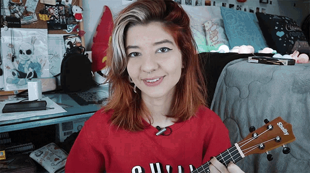 a woman in a red shirt is holding a ukulele