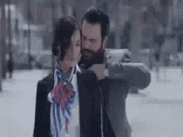 a man and a woman are kissing in the snow . the woman is wearing a scarf .
