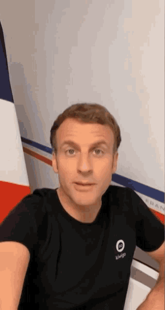 a man wearing a black t-shirt with the letter o on it is sitting in front of a french flag