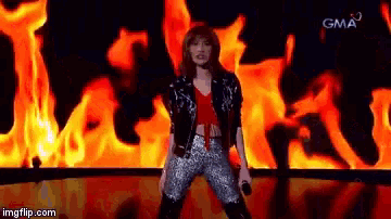 a woman singing in front of a fire with gma on the bottom right