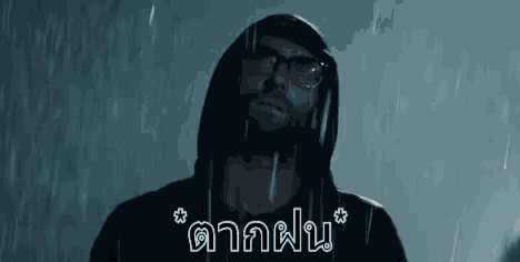 a man wearing a hoodie and glasses is standing in the rain .
