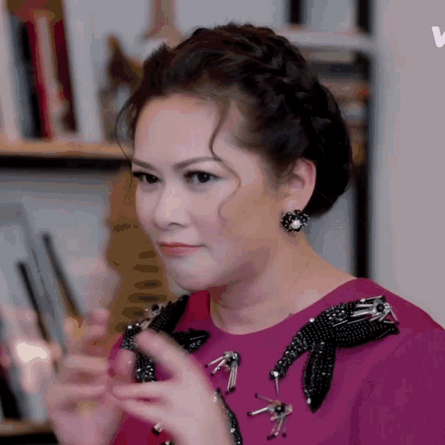a woman wearing a pink dress and black earrings looks at herself in the mirror