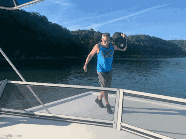 a man in a blue tank top is standing on a boat holding a baseball cap