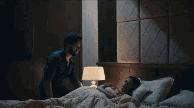 a man is standing next to a woman in a bed .