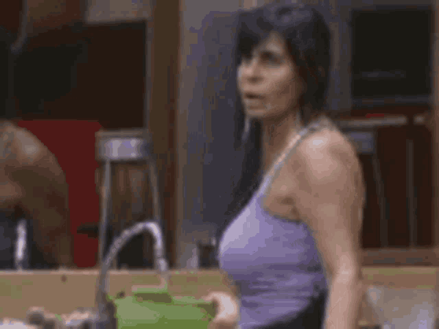 a woman in a purple tank top is standing in a kitchen holding a bowl .