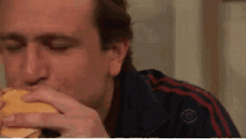 a man is eating a hamburger while wearing a cbs jacket