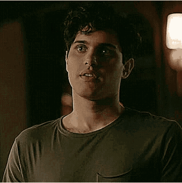 a young man in a green t-shirt is standing in a dark room looking at the camera .