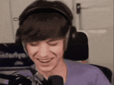 a young man wearing headphones is sitting in front of a microphone and smiling .