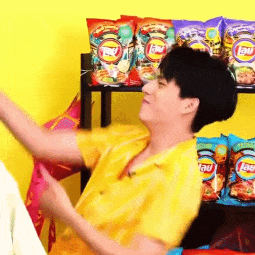a man in a yellow shirt is sitting in front of a shelf full of bags of lays chips .