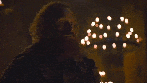 a man with a beard is standing in front of a chandelier in a dark room