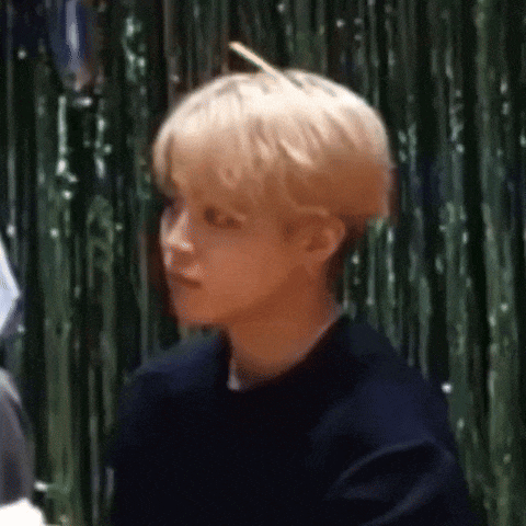 a young man with blonde hair is sitting in front of a green curtain and looking at the camera .