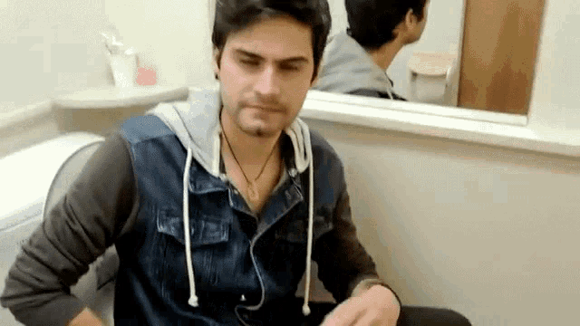 a man in a denim jacket is sitting in a bathroom