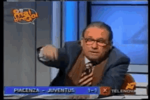 a man in a suit and tie is sitting in front of a television screen that says juventus