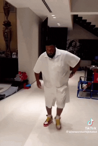 a man in a white shirt and shorts is dancing in a room with stairs in the background .