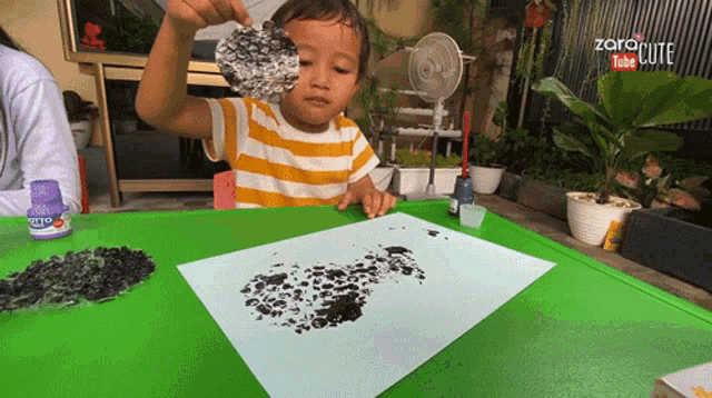 a child is playing with a piece of aluminum foil on a piece of paper with a bottle of glue nearby